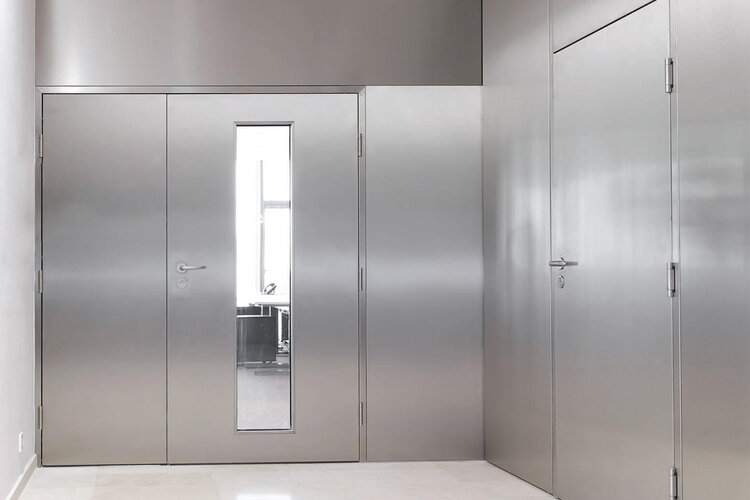 Moderner, heller Flur mit mehreren silbernen Metalltüren und einem Fluchtausgangsschild an der Decke