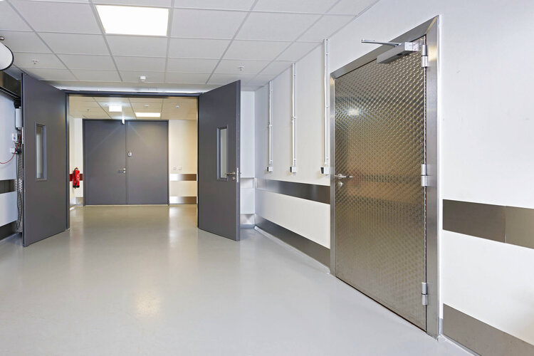Heller, moderner Krankenhaus- oder Technikflur mit geöffneten Doppeltüren und einer robusten Edelstahltür auf der rechten Seite